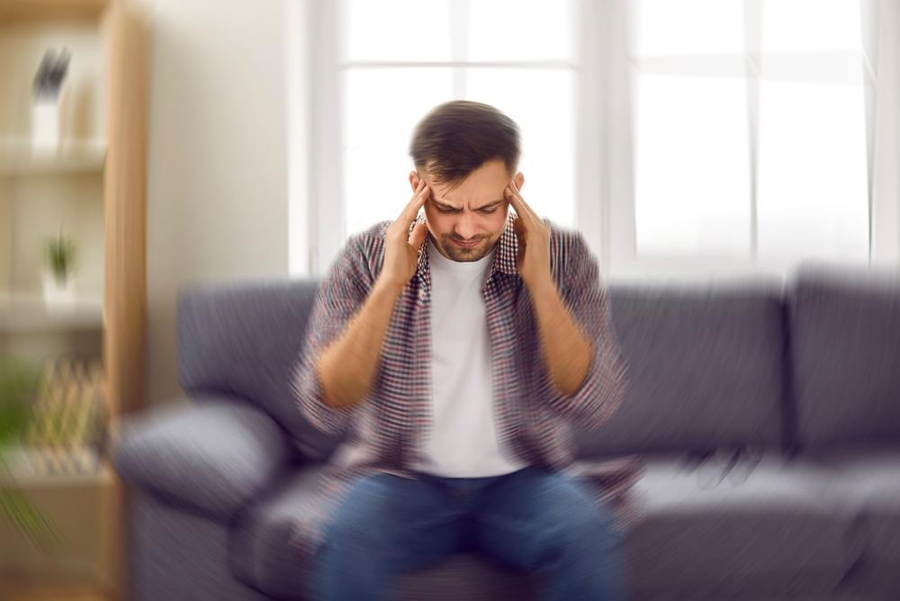 A man on his couch, holding his head, wondering what the average traumatic brain injury settlement is.