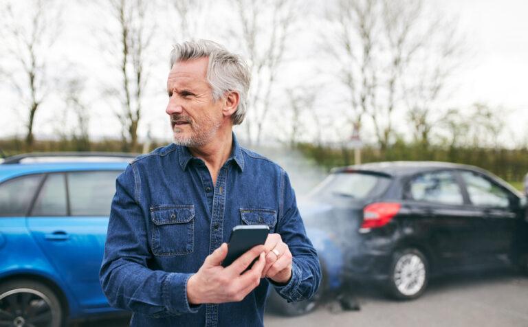 A man on his phone after a car accident, wondering if his insurance will cover him after an uninsured driver.