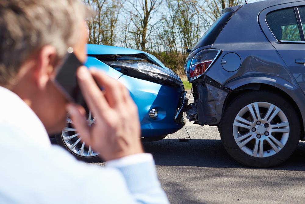 Man stands next to two crashed cars while on the phone with his lawyer to ask how to get a car crash report in Layton, UT.