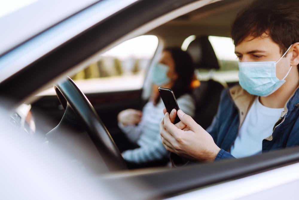 An Uber driver on their phone with a passenger in their car, wondering who you can sue after an Uber accident.