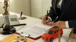 Lawyer filling out a claim form with a toy car sitting on his desk to symbolize the question of whether you can file a car accident lawsuit without an attorney.