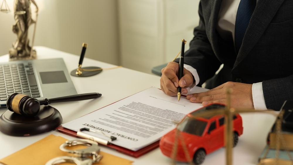 Lawyer filling out a claim form with a toy car sitting on his desk to symbolize the question of whether you can file a car accident lawsuit without an attorney.