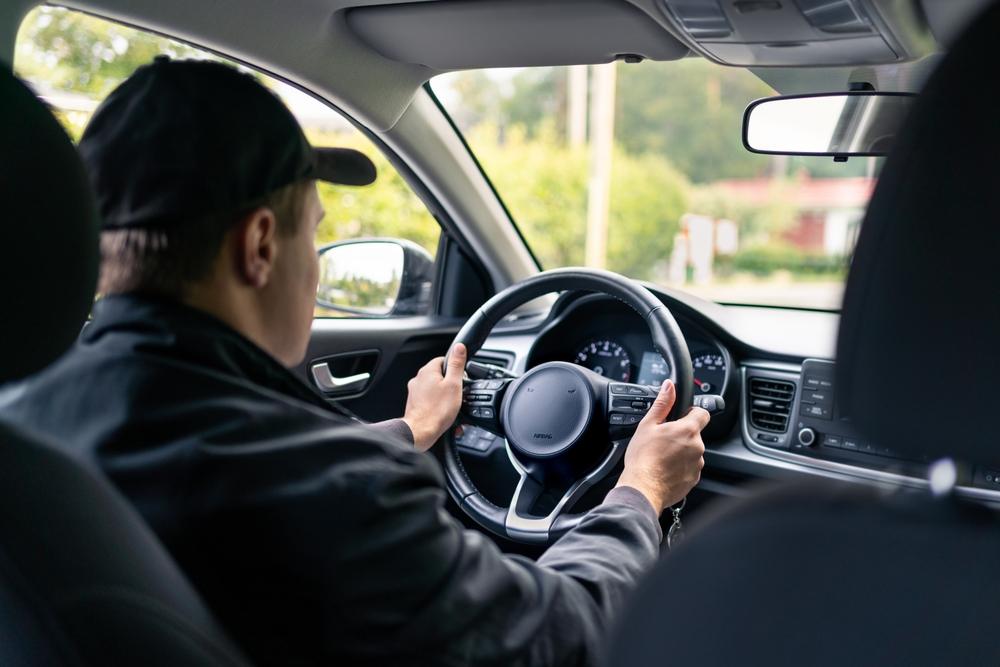 The back of a male rideshare driver’s head as he transports someone, leaving the passenger to wonder how insurance works in a rideshare accident.