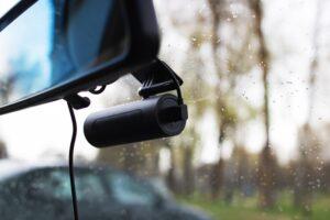 Close-up image of a dashboard camera hanging from a car’s rearview mirror, leaving other road users to wonder how to access Tesla dashcam footage after an accident.