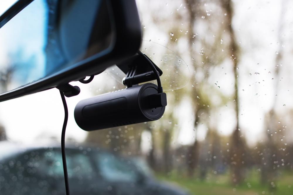 Close-up image of a dashboard camera hanging from a car’s rearview mirror, leaving other road users to wonder how to access Tesla dashcam footage after an accident.