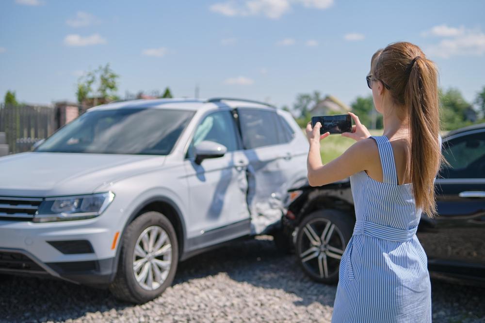 Woman uses her phone to take photos of the damage to the side of her vehicle before she asks how to get a car crash report in Ogden, UT.