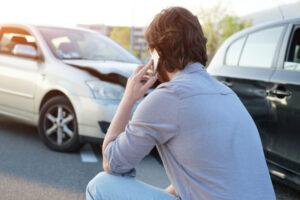 A driver sits in front of his crashed car while making a phone call to ask about how to get a car crash report in Spokane, WA.