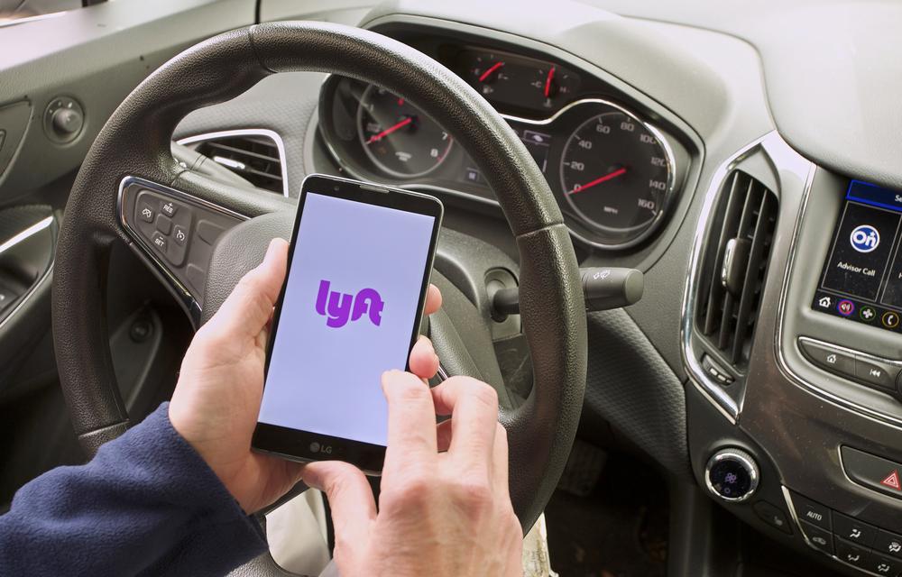 Someone sits in the driver’s seat of a car with the Lyft app open on their phone as they wonder about the average Lyft accident settlement.