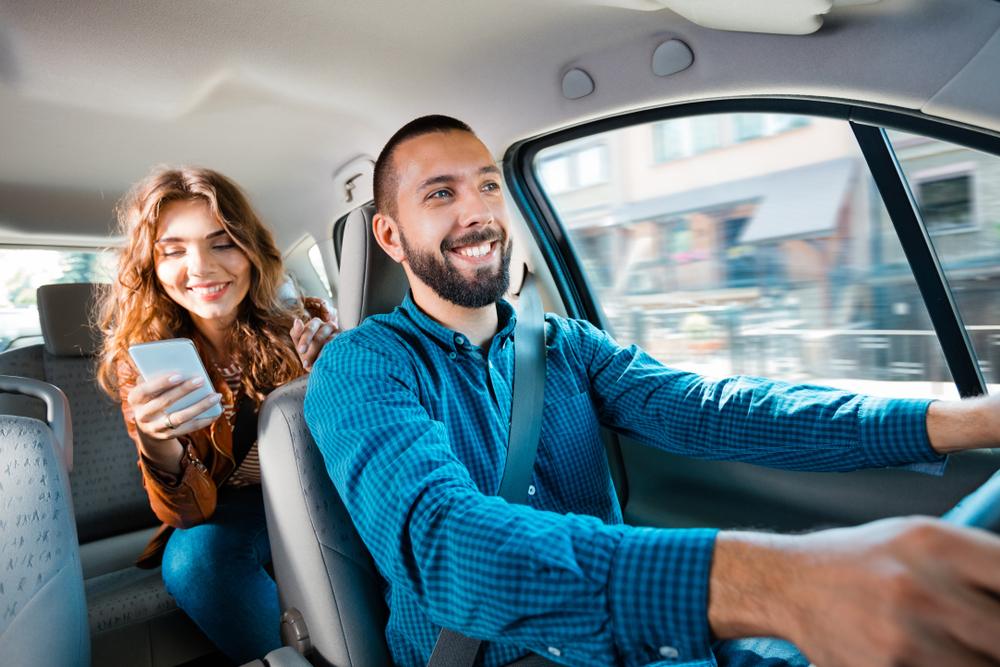 A woman in the backseat and a driver sitting and smiling in a rideshare vehicle as both wonder about the average Uber accident settlement.
