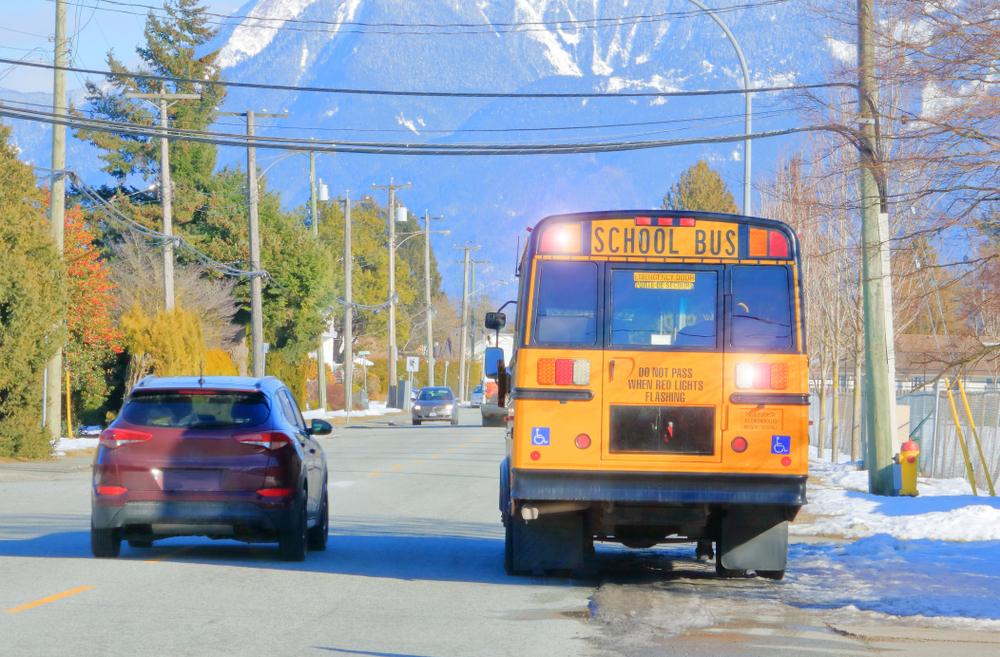 Yellow school bus pulled over on the side of the road next to a car, leaving the car driver to wonder what happens if a school bus gets into an accident.