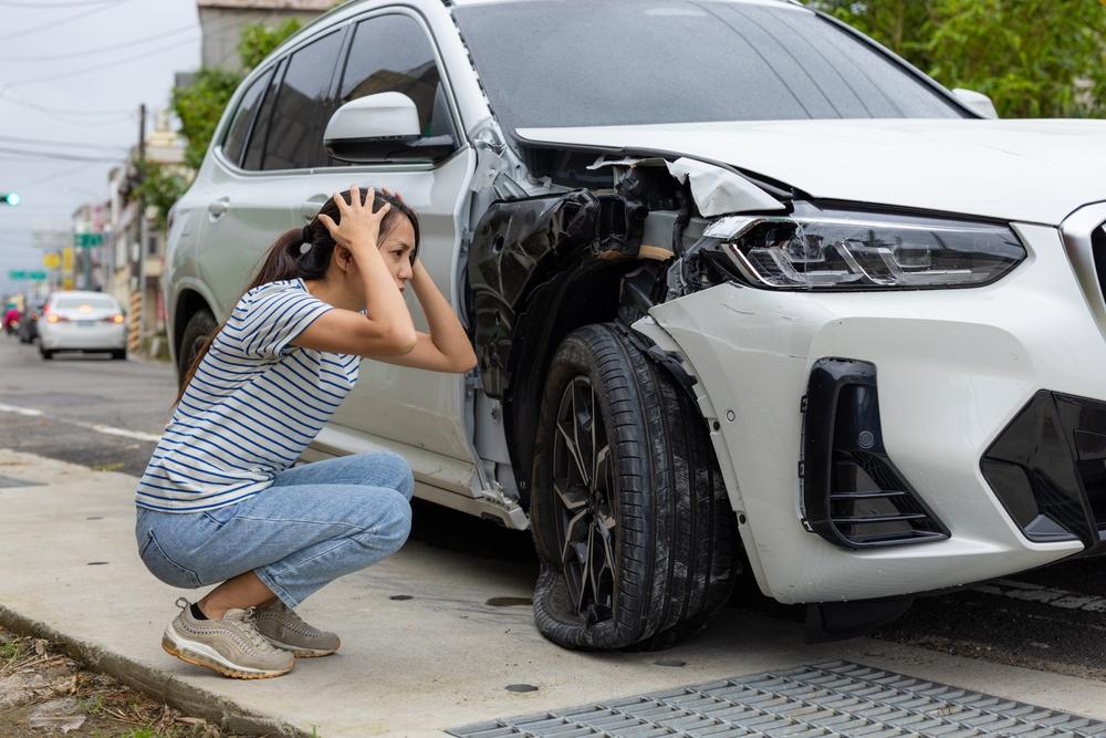 Woman looking at the damages to her car after a car crash, wondering about the car accident statute of limitations in Idaho.