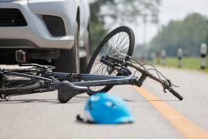 A crashed bicycle on the road with a blue helmet in front of it and a car in the background. What to do if a bicyclist causes a car accident.