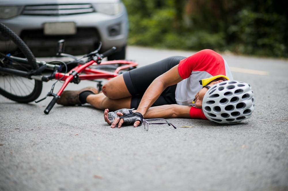 An injured cyclist on the ground after a bicycle accident, wondering what to do.