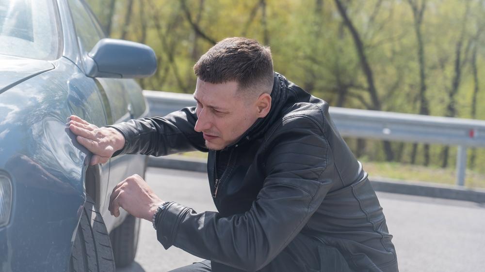 A man looking at his damaged car, wondering if you can sue for more than policy limits in Idaho.